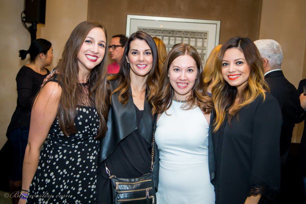 Group of four women posing for a picture, wearing cocktail dresses.